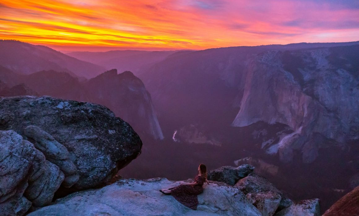 Asya Olson, traveler, lying on a rock while admiring the sunset on the horizon in Taft Point in Yosemite National Park during the fall season. The view overlooks many of the rock structures of the park.
